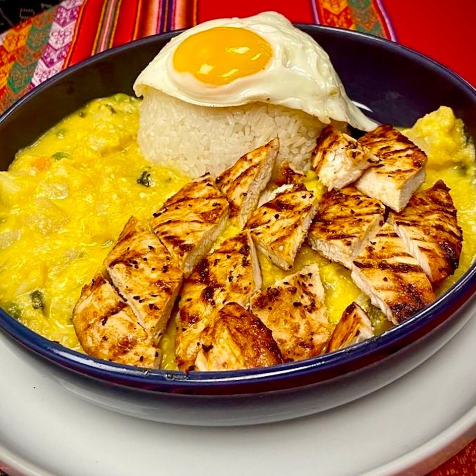 Peruvian Aji de Gallina with grilled chicken, rice, and a fried egg in a blue bowl.